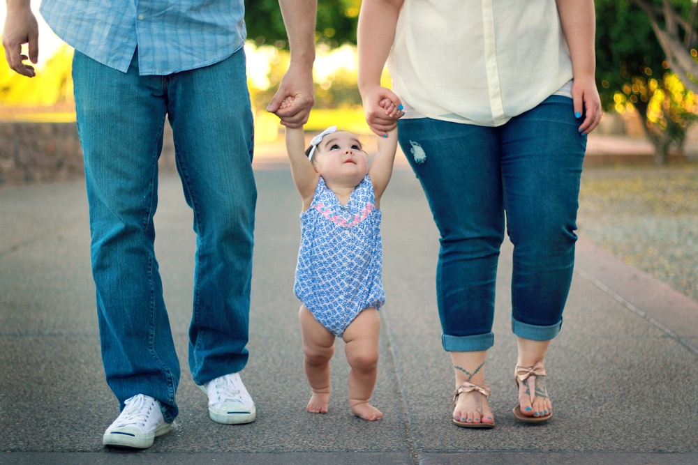 man and woman holding baby's hand while walking on road